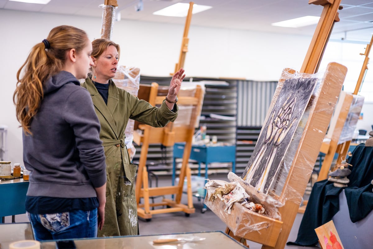 A professor gives feedback to her student next to her on her painting