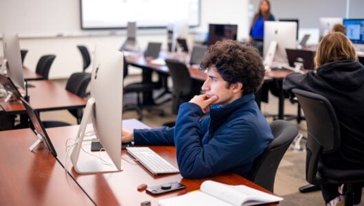 A student is seated at an imac and works on his project in typography class