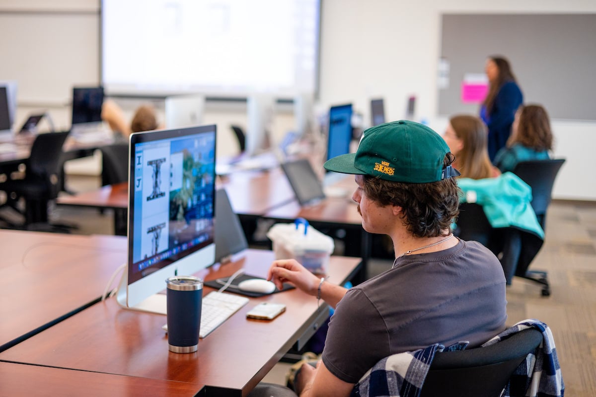 A student is seated at an imac and works on his project in typography class