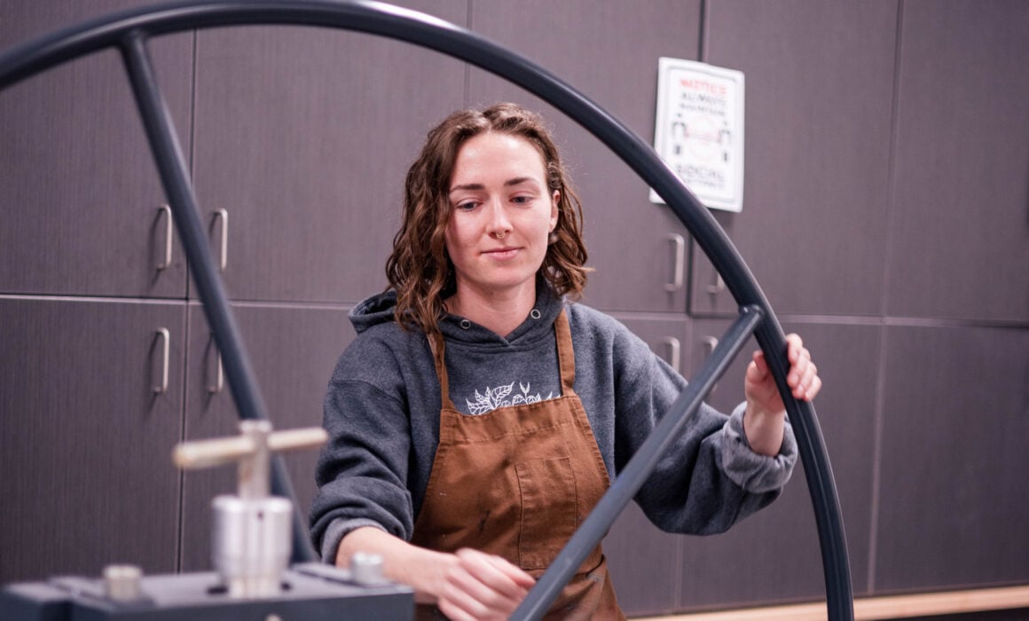A student wearing an apron spins a printmaking wheel.