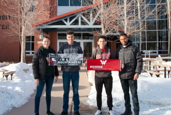 A couple of students and their parents pose for a photo with banners that say "I'm a Mountaineer" and "#IChoseWestern".