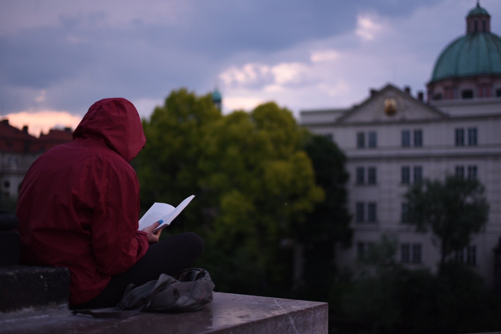 A student reads a book while sitting on a stone block in Prague.