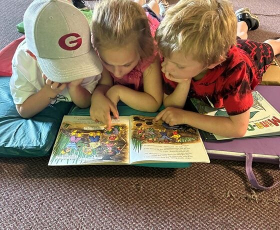 Three kids laying on the floor reading a book.