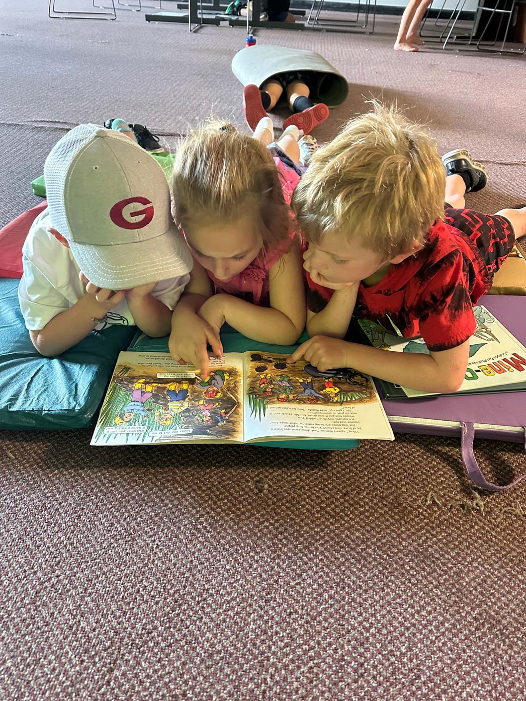 Three kids laying on the floor reading a book.