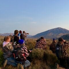 Students in the field use binoculars to observe surroundings.