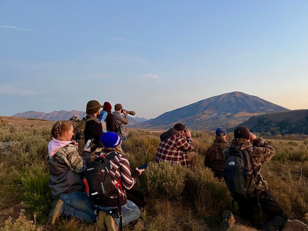 Students in the field use binoculars to observe surroundings.