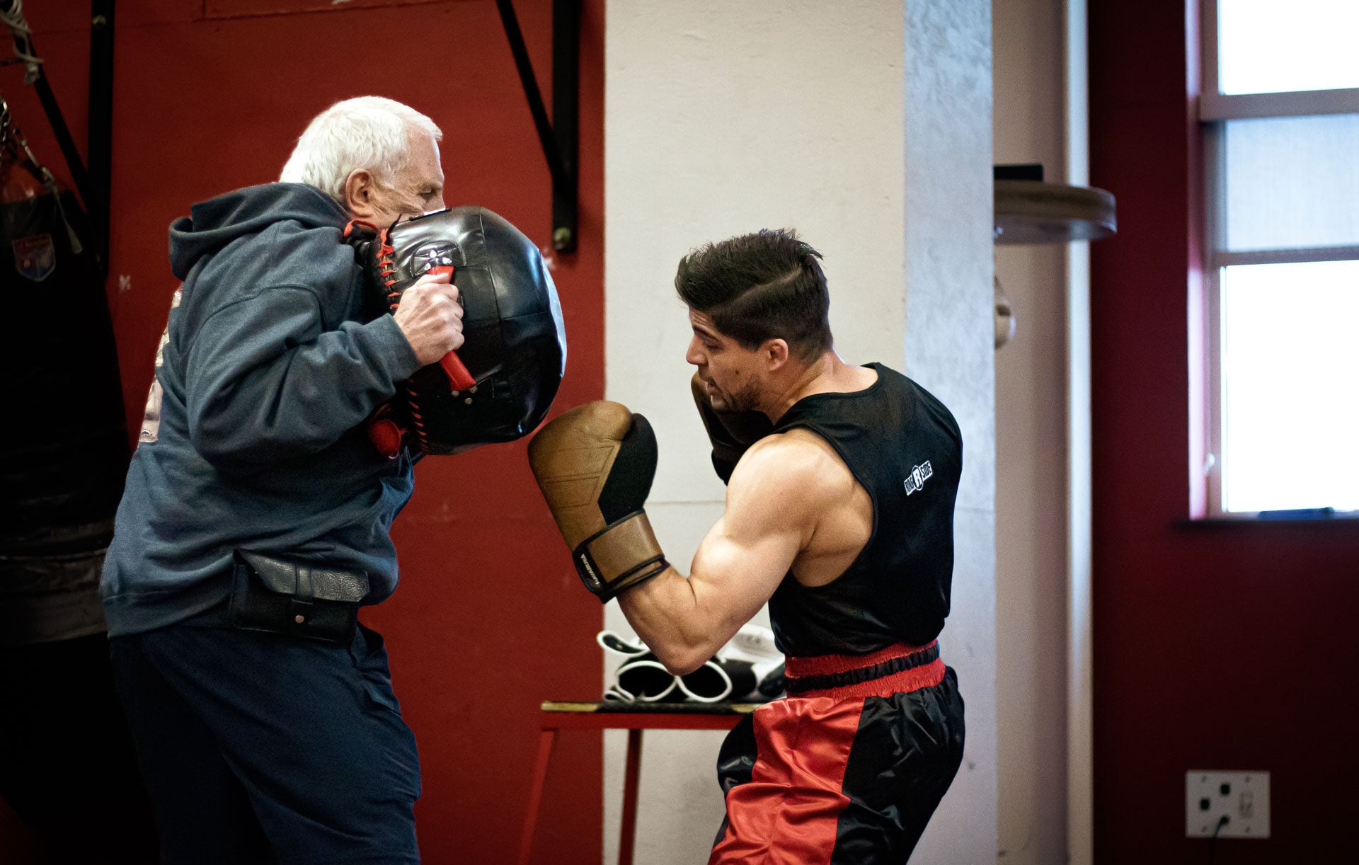 A boxer throws an uppercut punch at punching bag held by the coach.