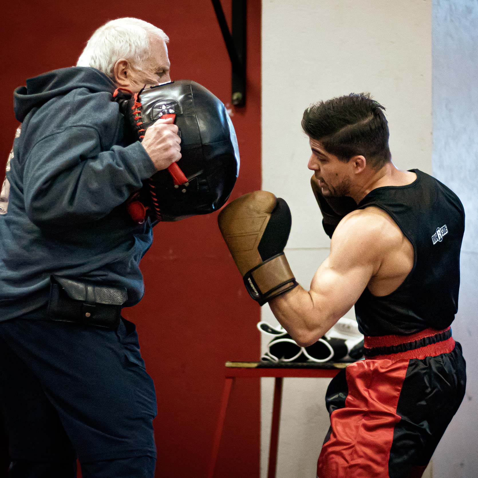 Male boxer throws an uppercut punch at punching bag held by the coach.