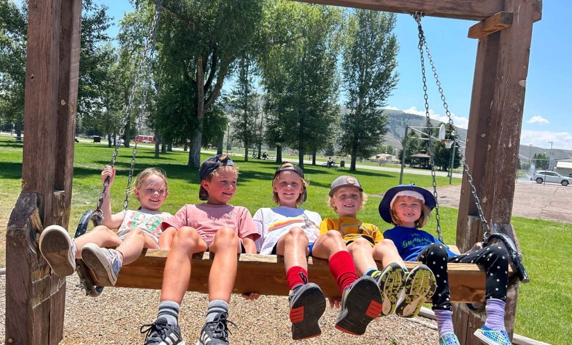 5 children attending a Junior Mountaineers summer camp on a wooden swing.