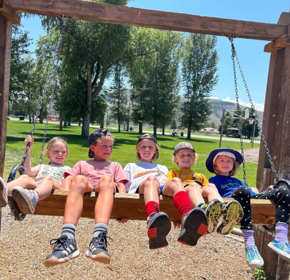 5 children attending a Junior Mountaineers summer camp on a wooden swing.