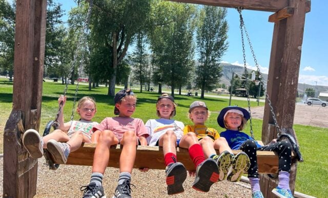 5 children attending a Junior Mountaineers summer camp on a wooden swing.