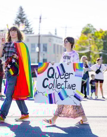 The LGBTQ+ club walks down Main Street with rainbow props and a sign that says "Queer Collective."