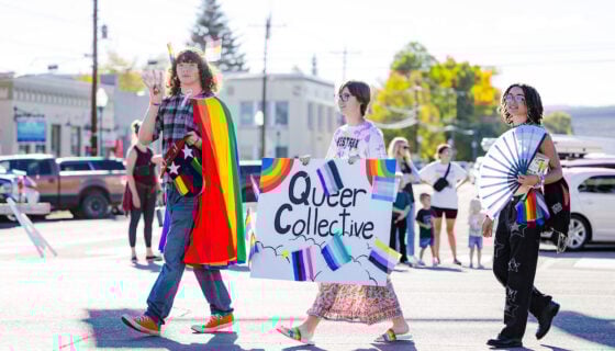 The LGBTQ+ club walks down Main Street with rainbow props and a sign that says "Queer Collective."