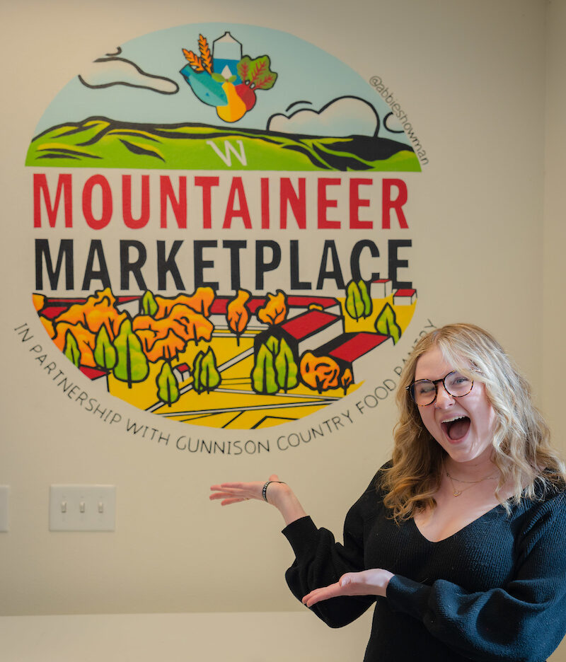 Abbie Showman - artist of Mountaineer Marketplace Mural stands in front of her work