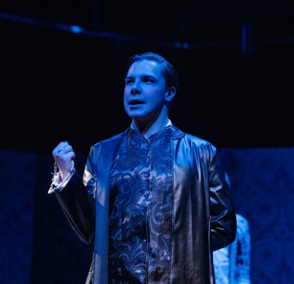 An actor looks up in moody blue light.