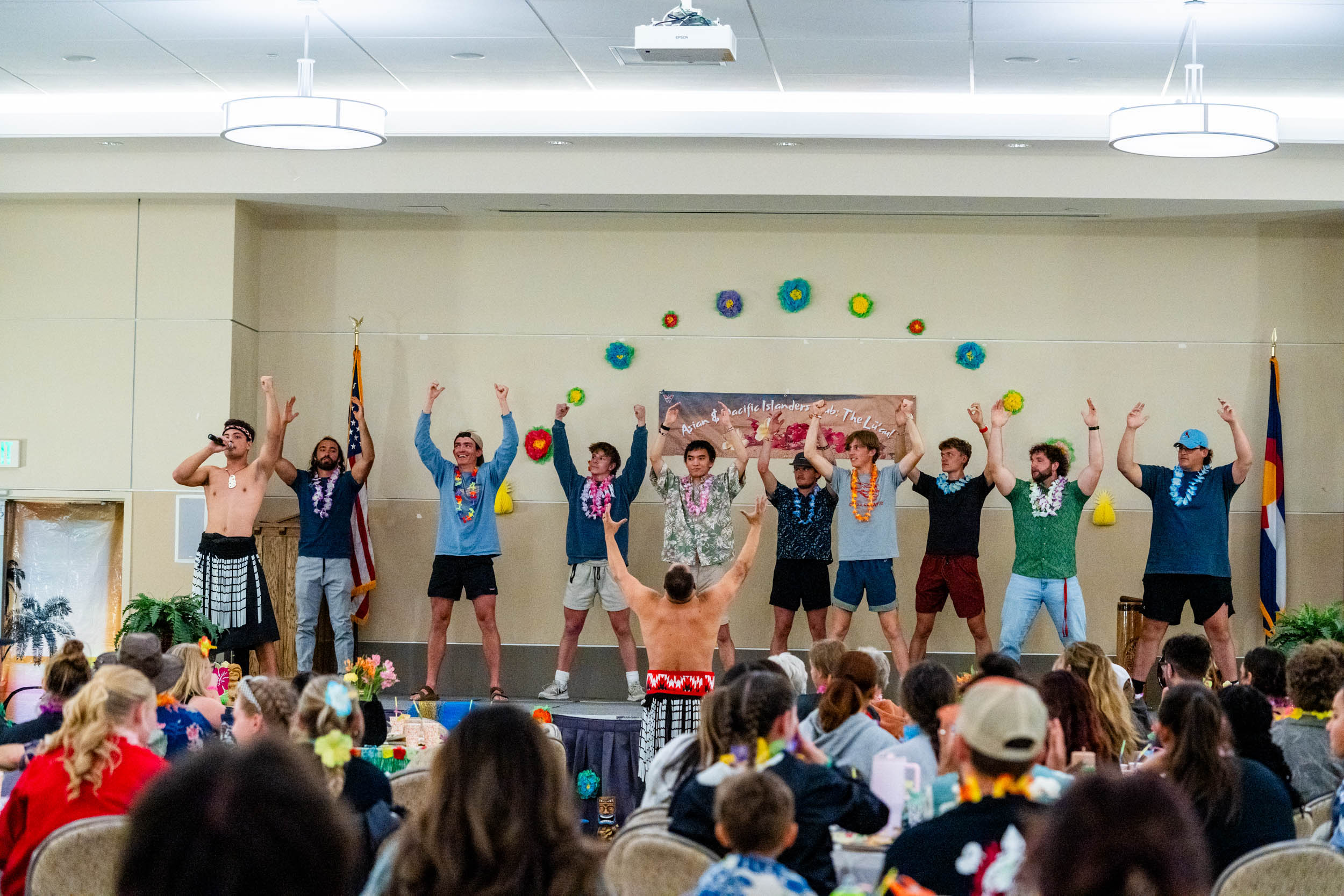 Students participate in preforming the Haka on stage at the 2025 Luau, with the audience in the foreground.