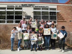 A group of students and kids holding up tote bags decorated for the Little Library.