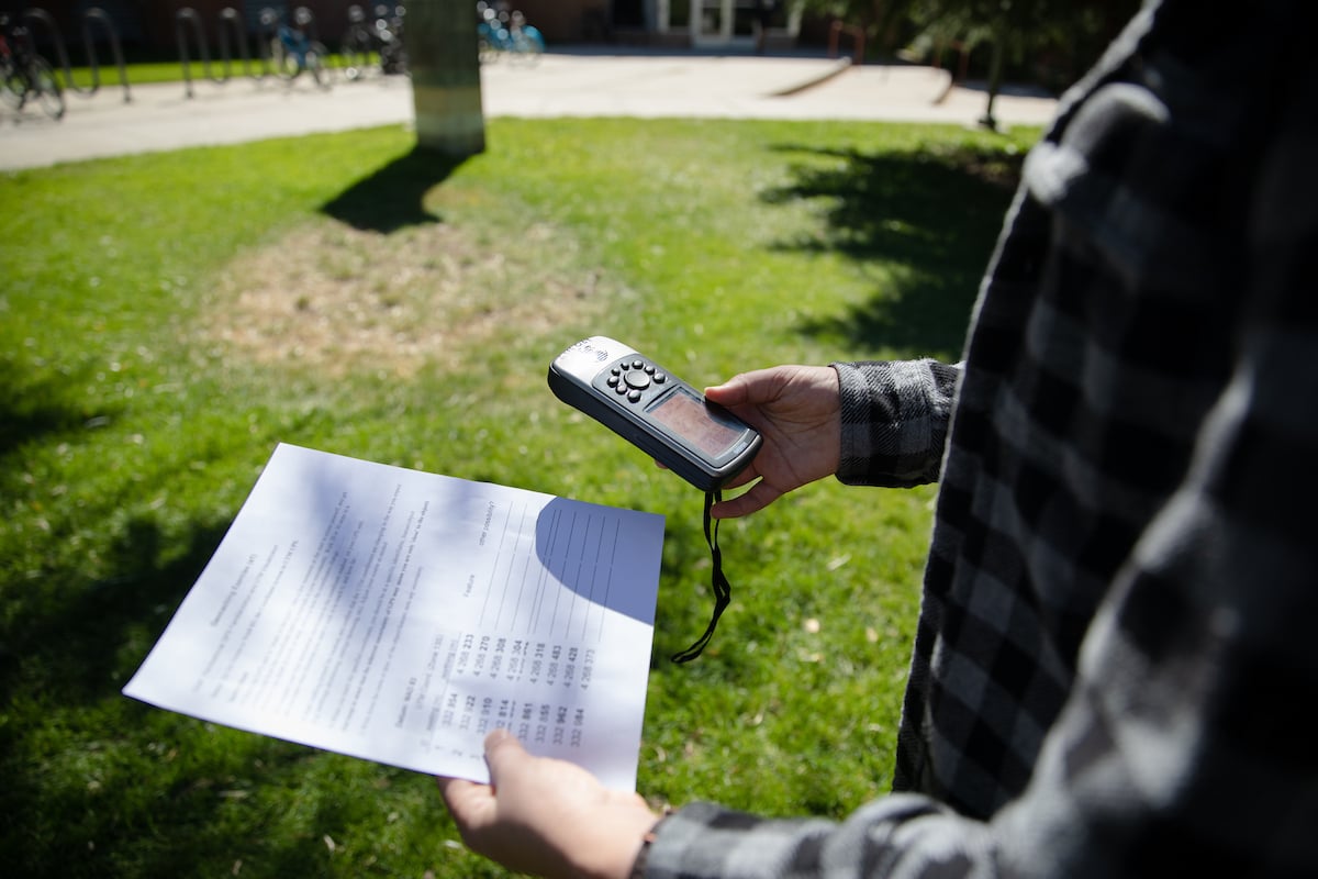 A photo of a student's hands holding a worksheet with coordinates and a GPS remote for an activity in the Our Digital Earth class.
