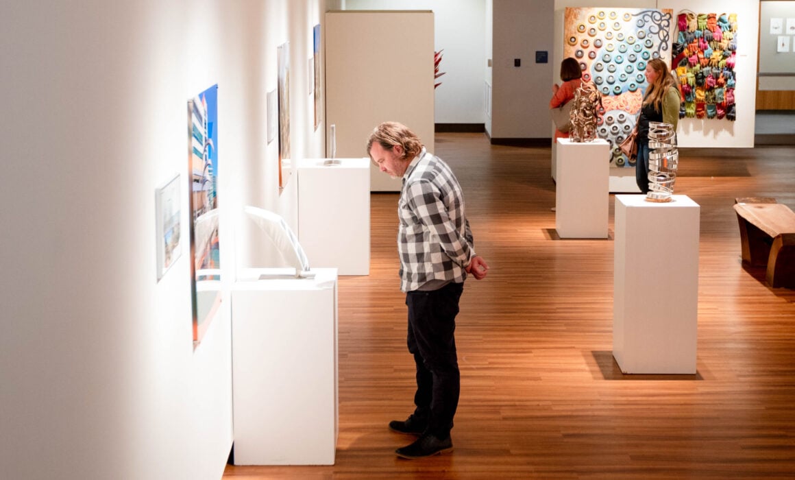 A man stands and admires a sculpture on a pedestal inside the Quigley Gallery.
