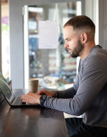 John Gonzales types on a laptop at Tributary Coffee for the ADC Photoshoot.