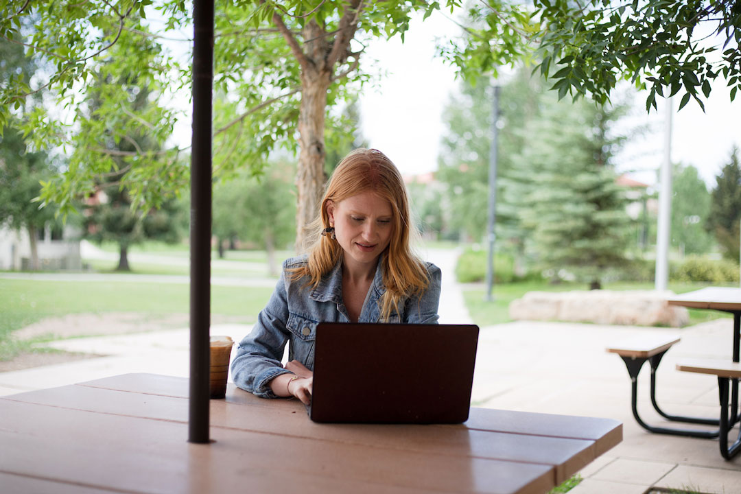 Mikay Elliot types on a laptop at a picnic table on the UC Patio.