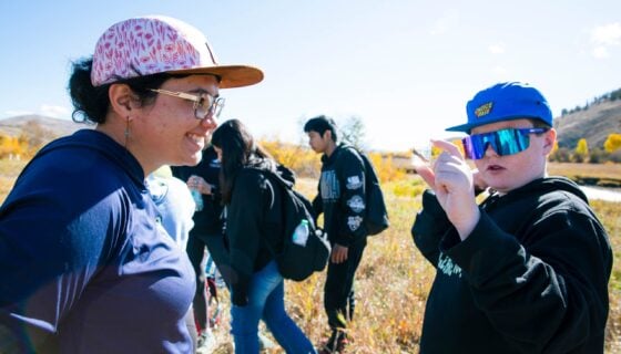 Ecology and Environmental Management graduate student, Sophia Reggiani, smiles as a boy holds up a small plastic vessel containing an aquatic insect in a sample of water.