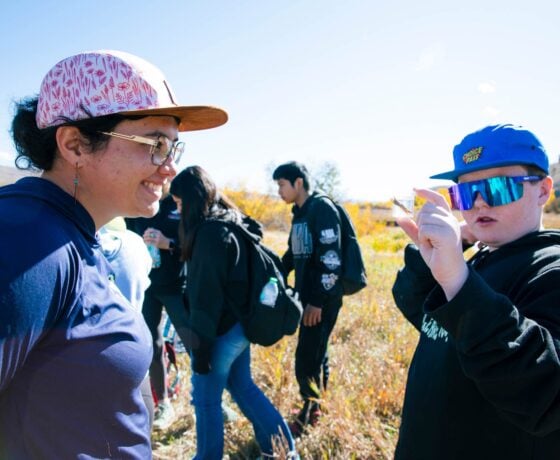 Ecology and Environmental Management graduate student, Sophia Reggiani, smiles as a boy holds up a small plastic vessel containing an aquatic insect in a sample of water.