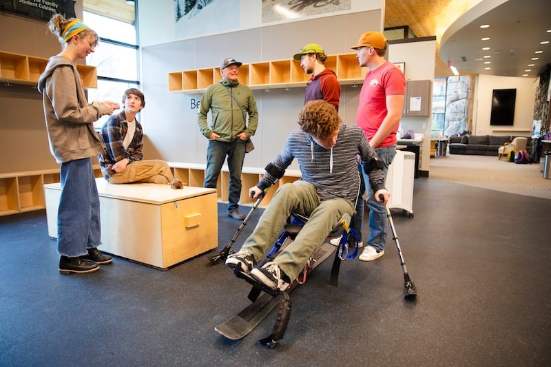 An ROE student tests out a sit ski at the Adaptive Sports Center while a few of his classmates observe.
