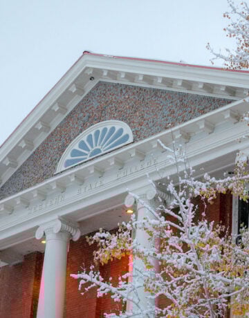 The top of the taylor hall building covered in snow surrounded in snowy fall leaves.