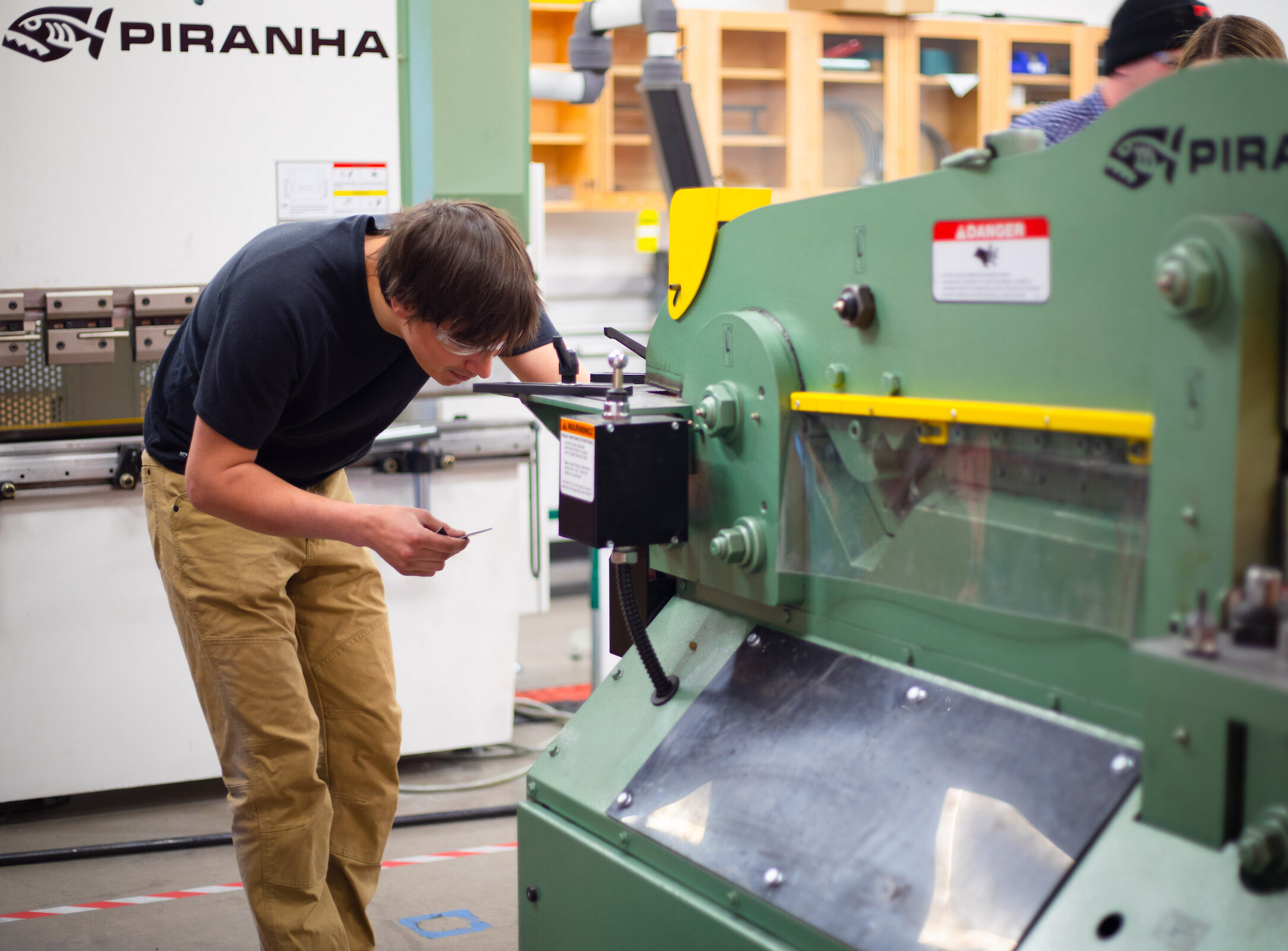 A student bends over to make an adjustment to a machine he's using in the Fabrication Shop of the Rady building.