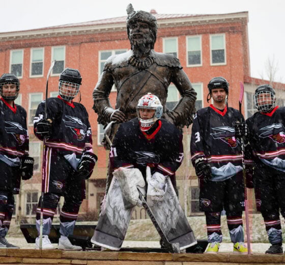 A photo of five Western Hockey players posing for a photo around the mountaieer statue while it snows.