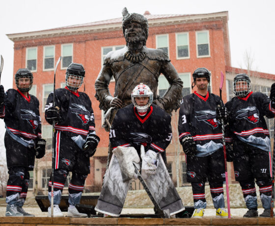 A photo of five Western Hockey players posing for a photo around the Mountaineer statue while it snows.