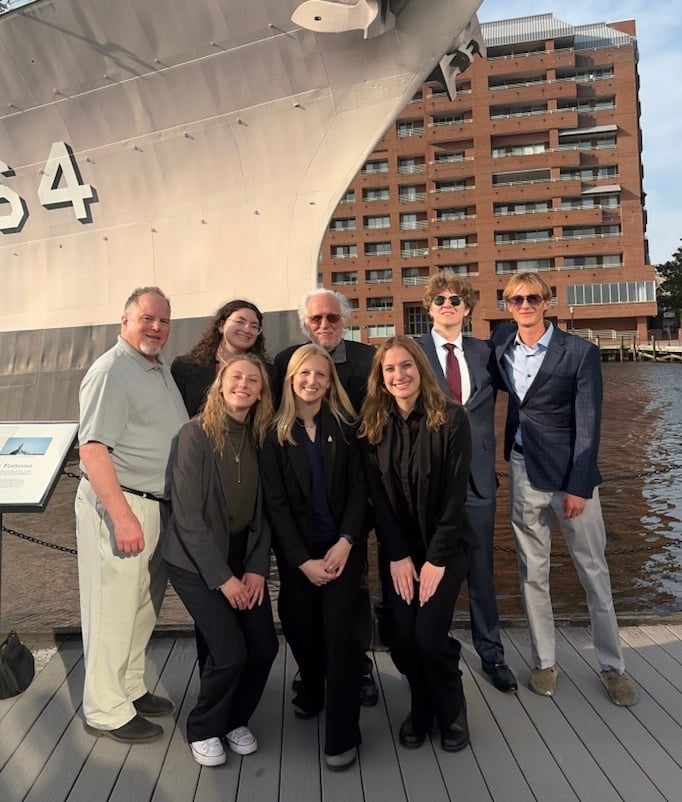 A group of business students and professors pose for a group photo in front of a large ship.