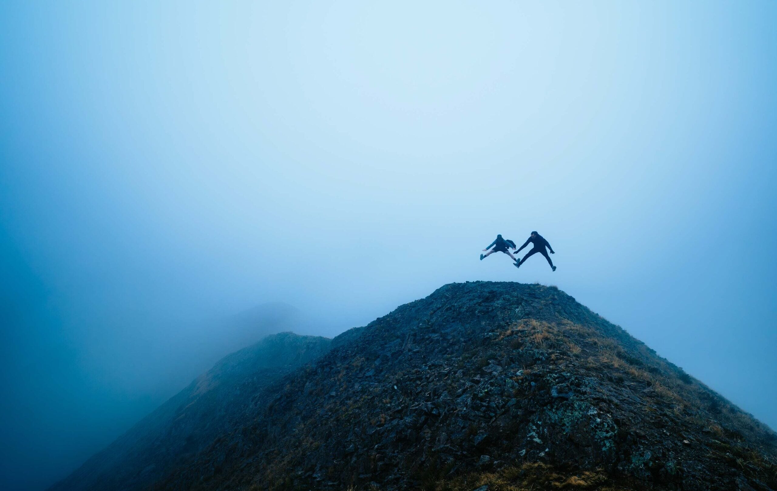 2 alumni jump on top of Gothic Mountain in the fog.