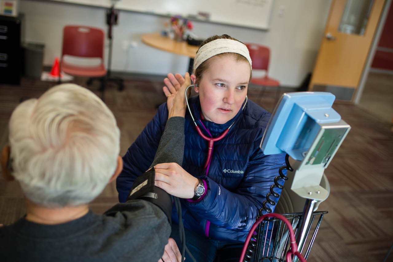 A student takes the blood pressure of a community member.