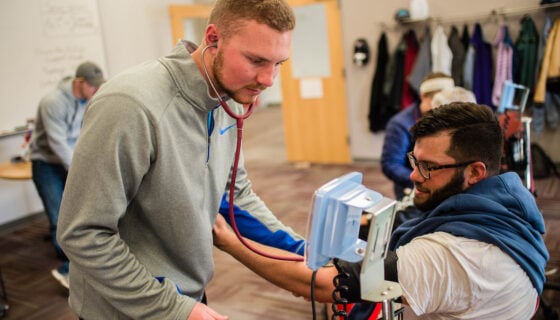 A student takes the blood pressure of a patient.