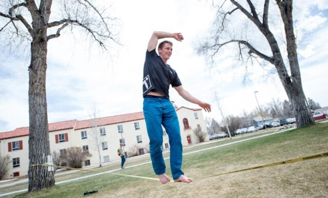 A student on a slack line in front of Ute Hall on Taylor Lawn.