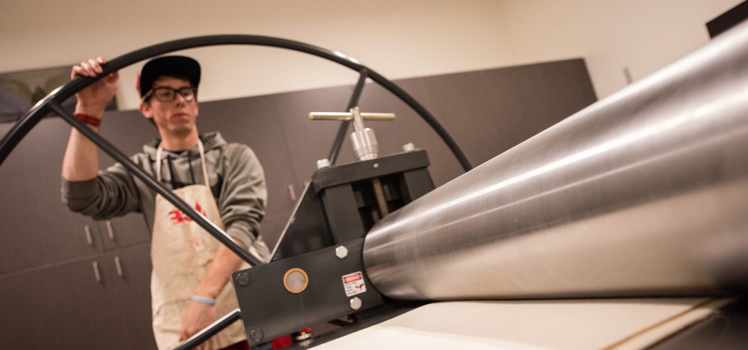 A student wearing an apron turns the wheel at a printmaking station.