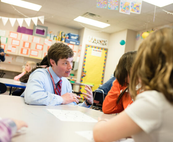 A student teacher assists elementary students in a classroom.