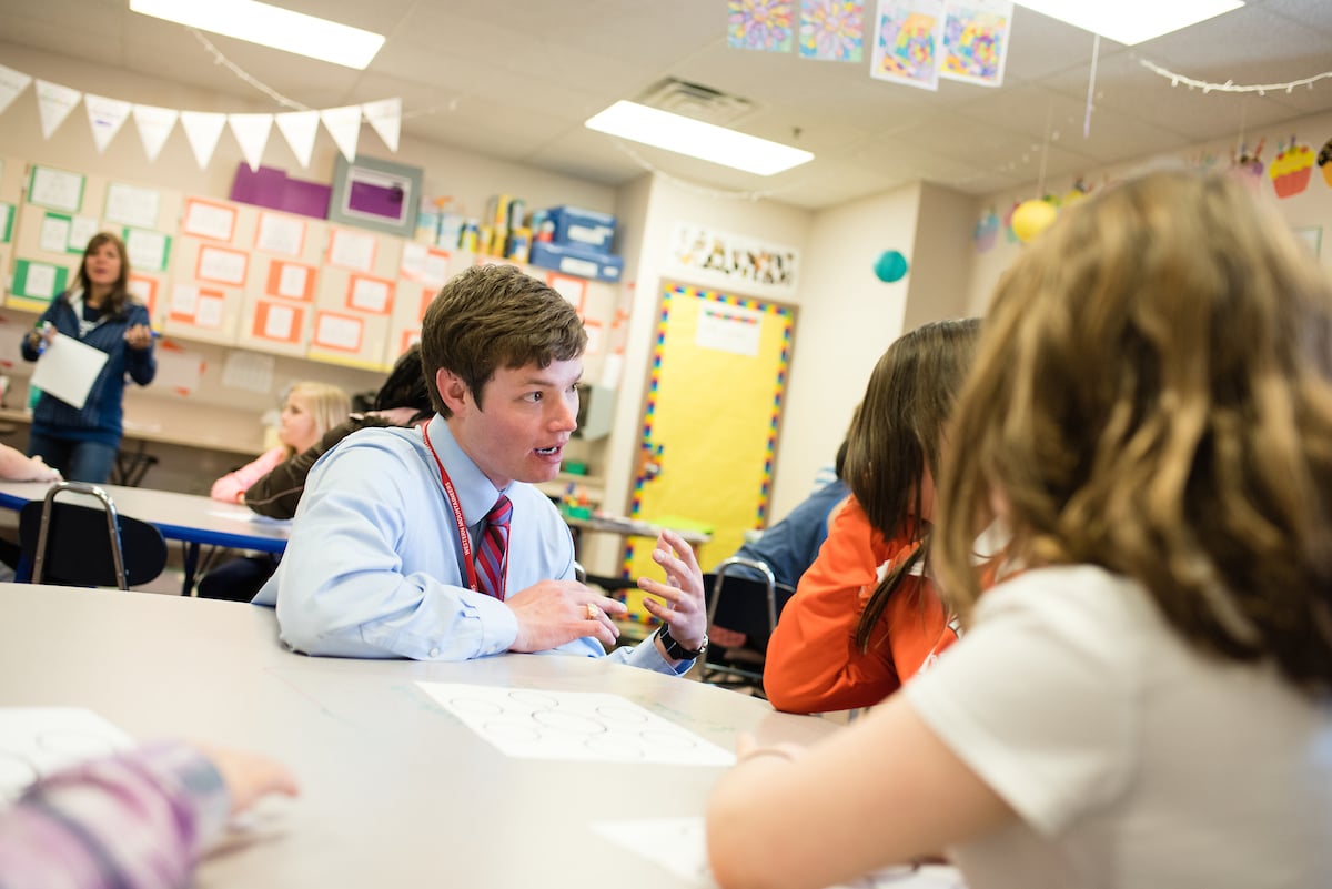 A student teacher assists elementary students in a classroom.