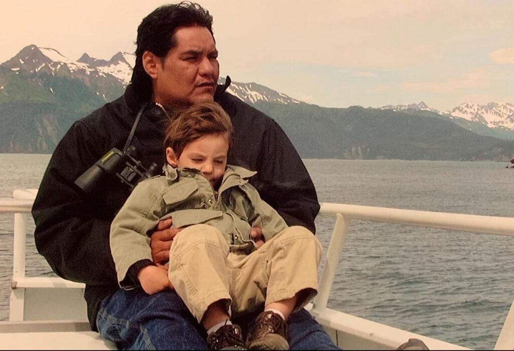 Sage as a little boy with his dad in front of a lake with mountains in the background