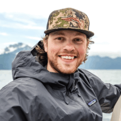 Headshot of Andrew Kunze on a boat in front of mountains.