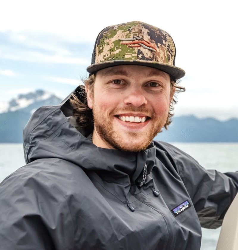 Headshot of Andrew Kunze on a boat in front of mountains.