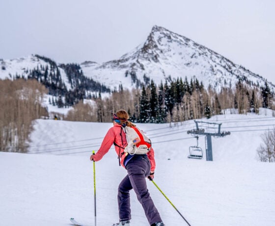A female Western skimo athlete skins up the uphill route at Crested Butte Mountain Resort with the peak of Mt. Crested Butte in the background.