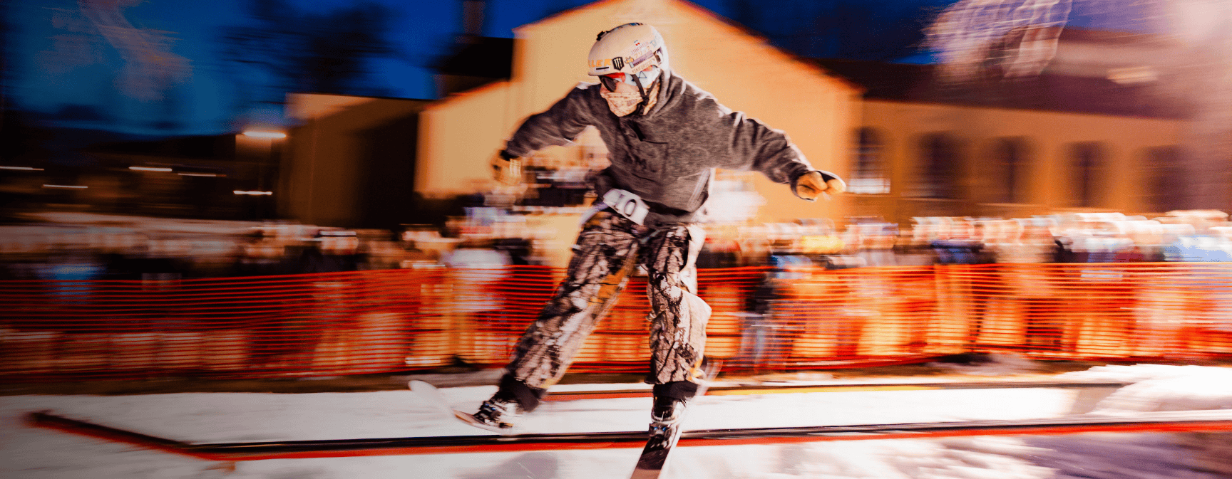 A skier slides a rail in front of the library while students cheer for him in the background. A motion blur effect is used in this photo.