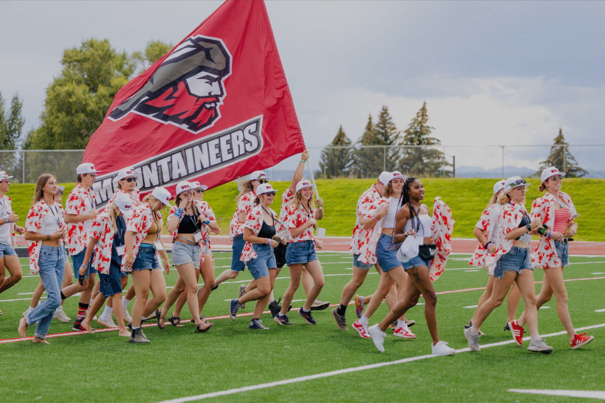 Orientation leaders wearing shirts with a lobster pattern run onto the football field with the Mountaineers flag during the orientation welcome.