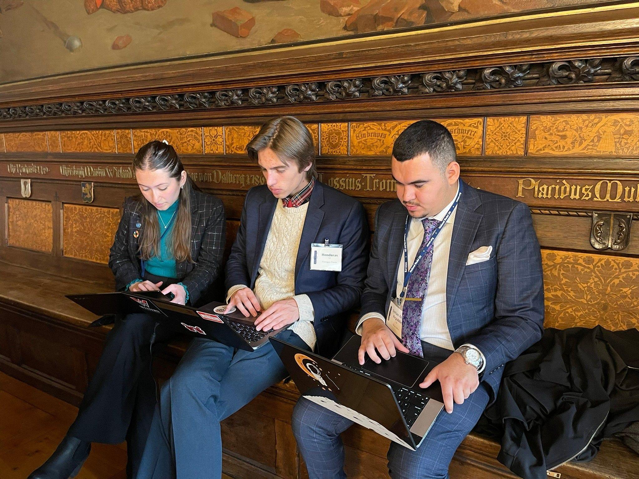 Three students type on laptops at the Model UN conference