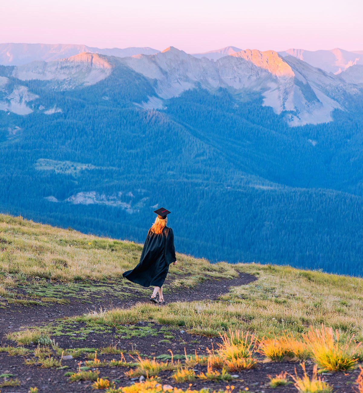 Student wearing a cap and gown walking down a high alpine ridgeline at sunrise