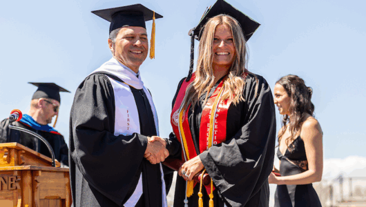 Taylor Hubbard shakes hands with President Brand Baca on the stage at commencement.