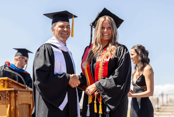 Taylor Hubbard shakes hands with President Brand Baca on the stage at commencement.
